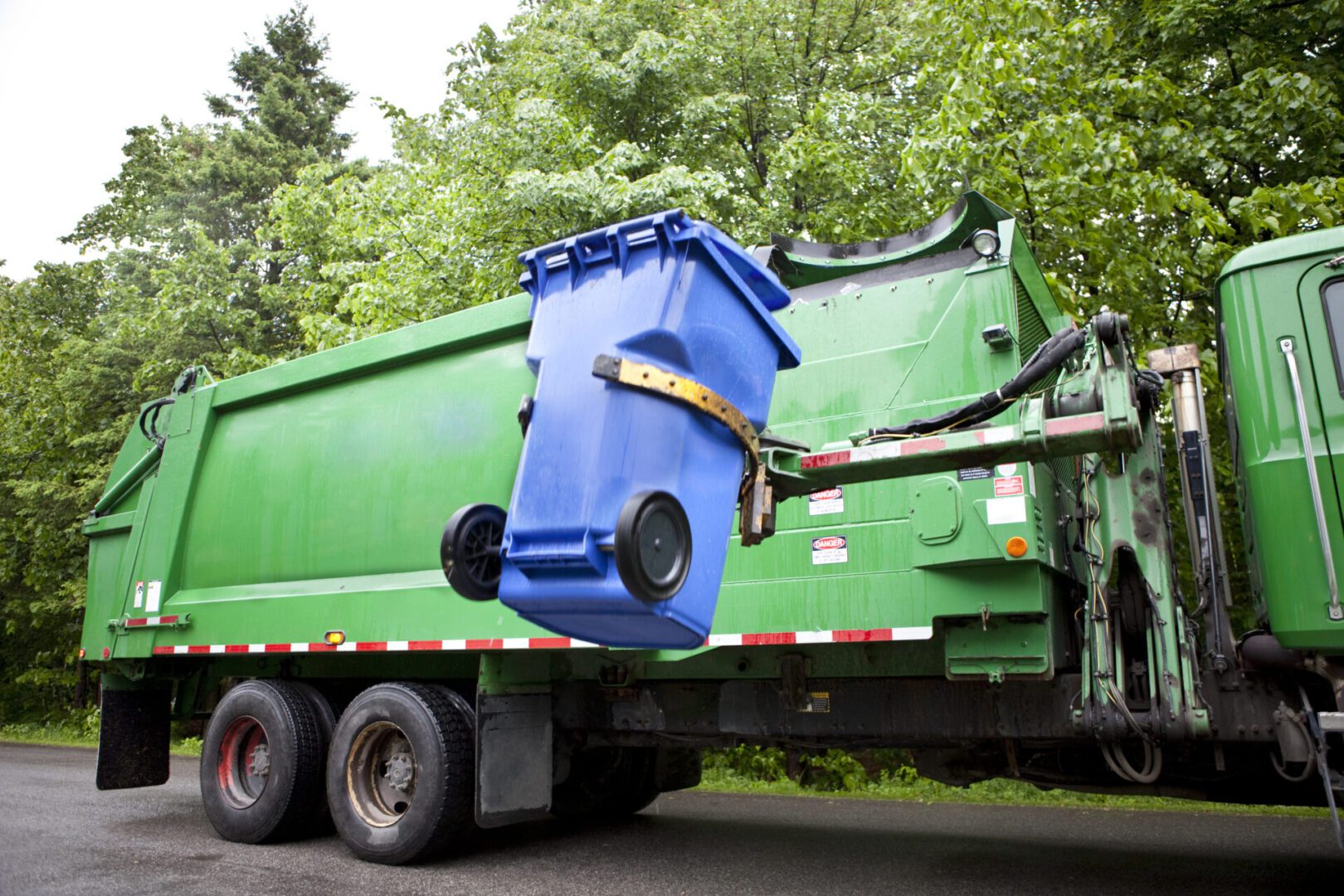 Garbage truck lifting blue recycling bin.