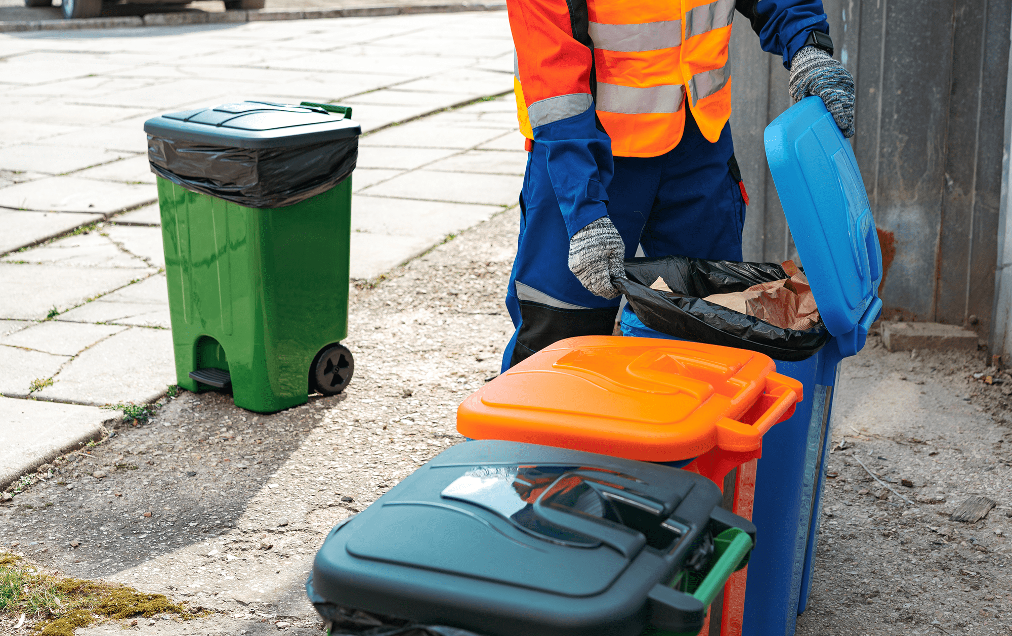 Worker sorting recycling bins on street.