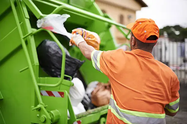 Sanitation worker loading garbage truck outdoors.
